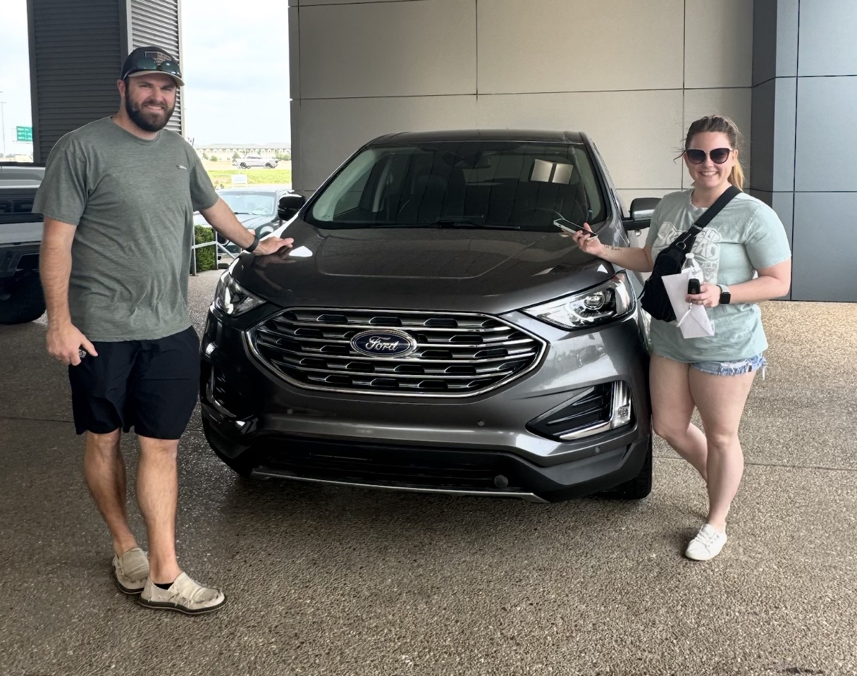 Two customers posing with their new charcoal gray Ford SUV