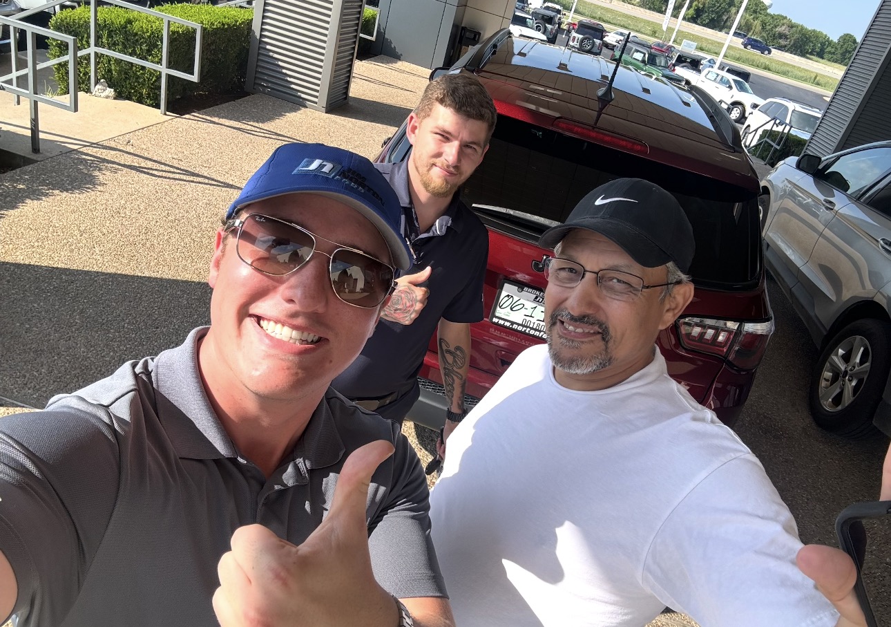 Three happy customers giving thumbs-ups next to a dark red SUV